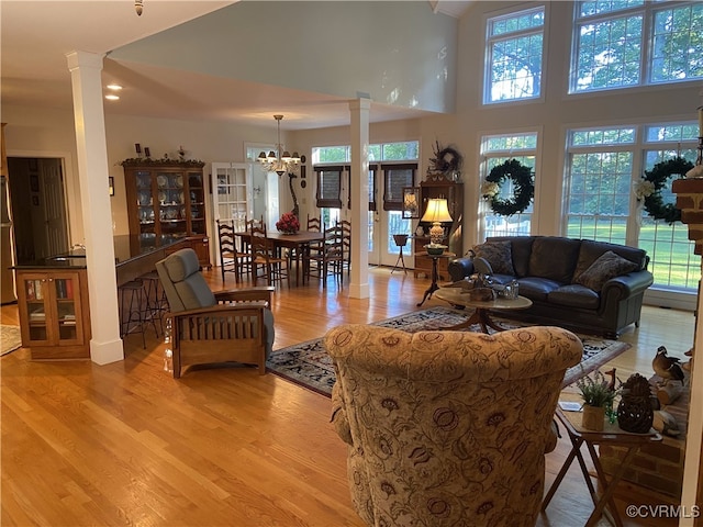 living room with a high ceiling, a notable chandelier, ornate columns, and light wood-type flooring