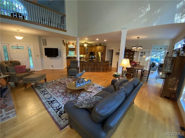 living room featuring a towering ceiling, decorative columns, a chandelier, and light hardwood / wood-style floors