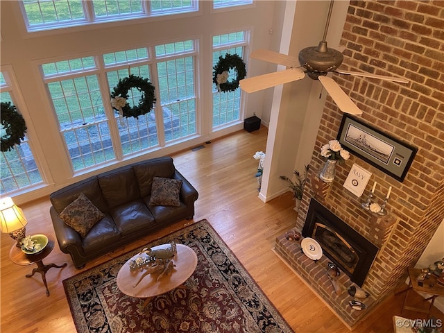 living room with a high ceiling, light hardwood / wood-style flooring, brick wall, a brick fireplace, and ceiling fan