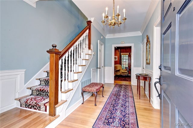 entryway with light hardwood / wood-style floors, an inviting chandelier, and ornamental molding