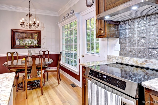 kitchen featuring ornamental molding, an inviting chandelier, stainless steel range oven, light hardwood / wood-style flooring, and wall chimney range hood