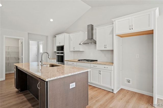 kitchen featuring wall chimney exhaust hood, an island with sink, sink, vaulted ceiling, and white cabinets