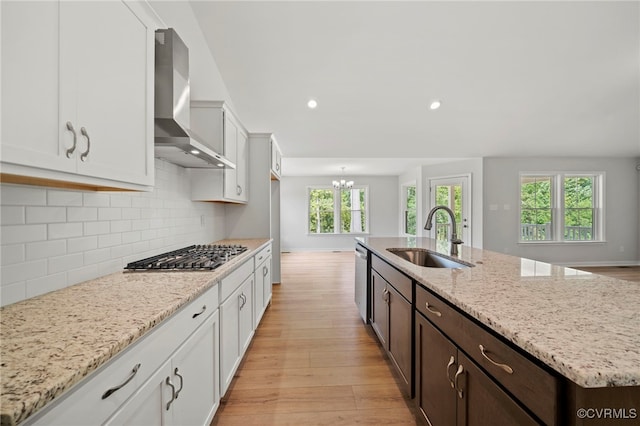 kitchen with a wealth of natural light, stainless steel appliances, light hardwood / wood-style floors, wall chimney exhaust hood, and sink