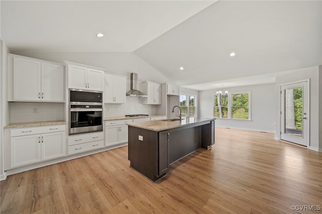 kitchen featuring light hardwood / wood-style floors, stainless steel appliances, vaulted ceiling, white cabinets, and a kitchen island with sink