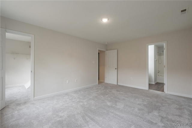 unfurnished bedroom featuring a walk in closet, ensuite bath, and light colored carpet