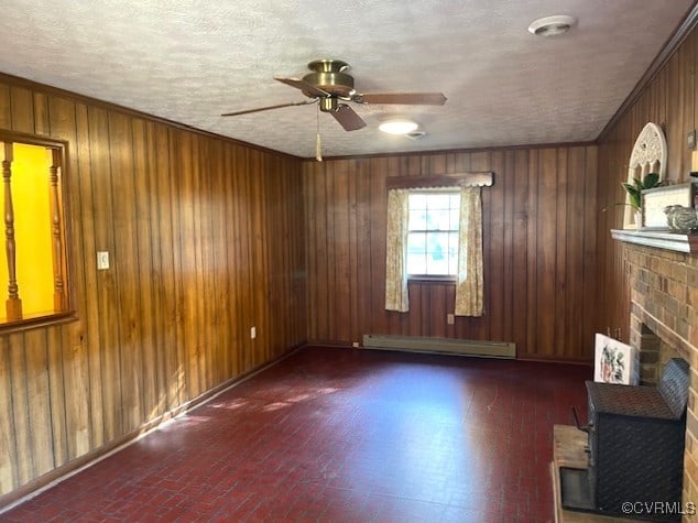 empty room featuring wooden walls, a baseboard heating unit, crown molding, a fireplace, and ceiling fan