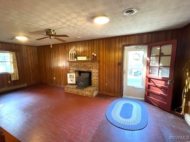 unfurnished living room with wood walls, a textured ceiling, a baseboard radiator, and ceiling fan