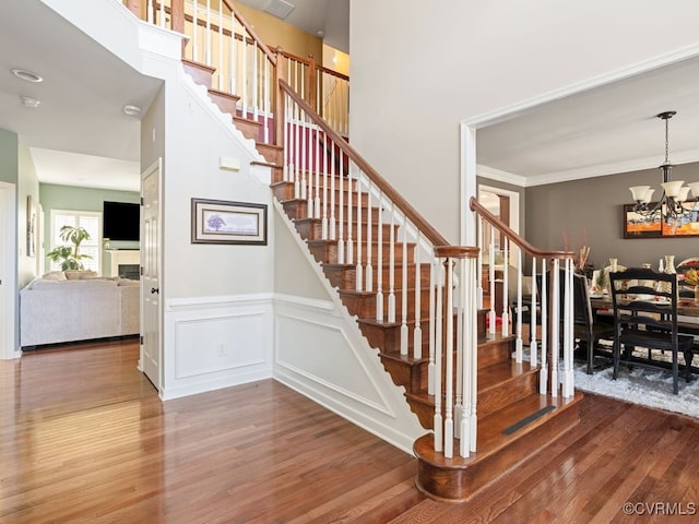 stairway with wood-type flooring, an inviting chandelier, and ornamental molding