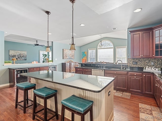 kitchen with a kitchen bar, dark hardwood / wood-style flooring, ceiling fan, sink, and a center island