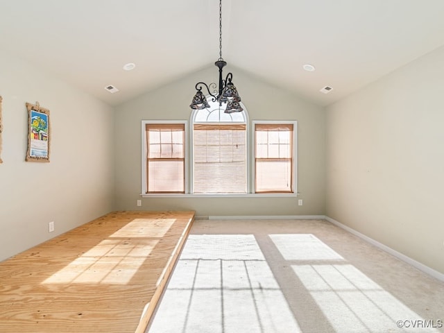 carpeted spare room featuring plenty of natural light, vaulted ceiling, and a chandelier