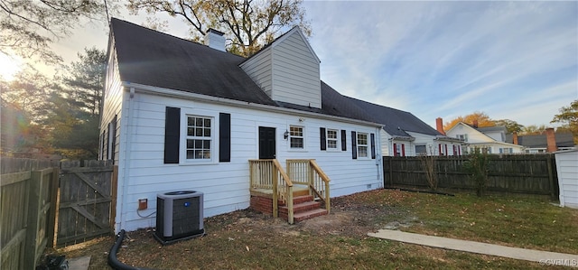 back house at dusk with central AC and a lawn