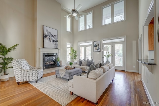 living room featuring french doors, ceiling fan, hardwood / wood-style floors, a fireplace, and a high ceiling