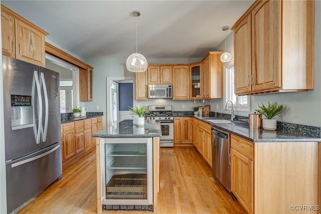 kitchen with sink, stainless steel appliances, dark stone countertops, pendant lighting, and light hardwood / wood-style floors