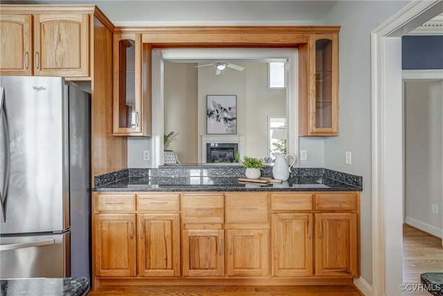 kitchen with dark stone countertops, stainless steel fridge, light hardwood / wood-style flooring, and ceiling fan