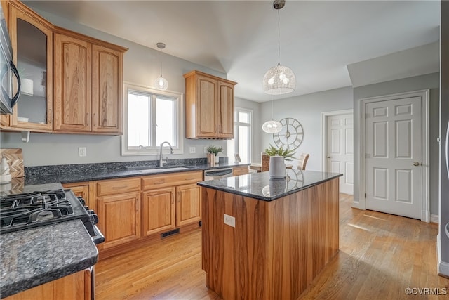 kitchen featuring light wood-type flooring, dark stone counters, sink, a kitchen island, and hanging light fixtures