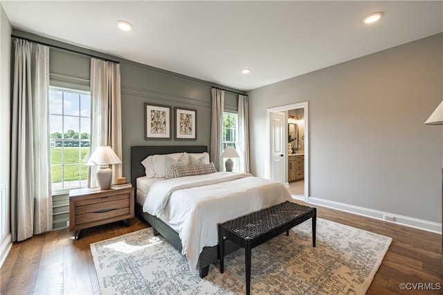 bedroom featuring ensuite bath, multiple windows, and dark hardwood / wood-style floors