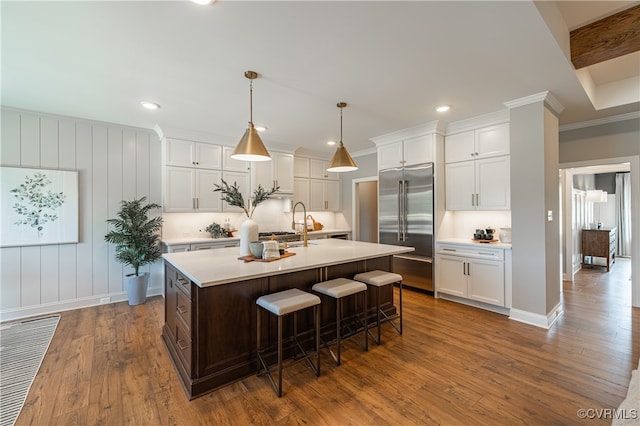 kitchen featuring dark wood-type flooring, white cabinetry, an island with sink, and built in refrigerator