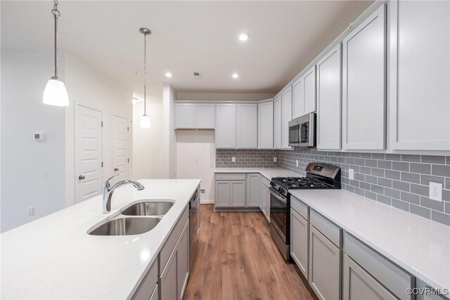 kitchen with wood finished floors, a sink, decorative light fixtures, appliances with stainless steel finishes, and decorative backsplash