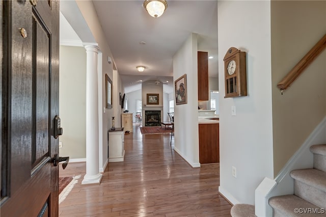 foyer featuring decorative columns, hardwood / wood-style floors, vaulted ceiling, and a fireplace