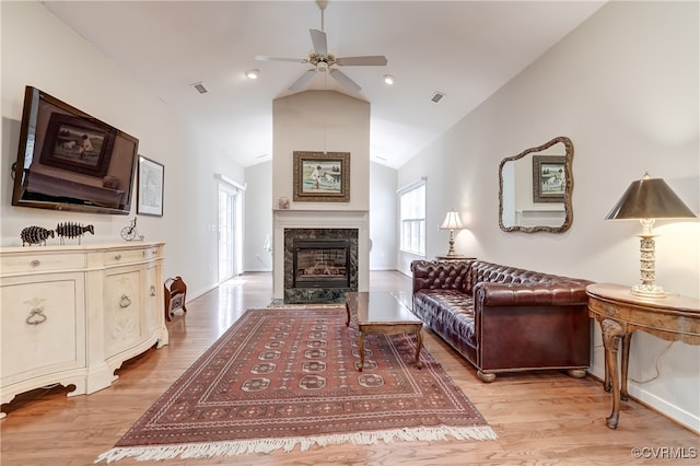 living area featuring light wood-type flooring, vaulted ceiling, a high end fireplace, and ceiling fan