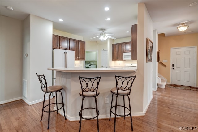 kitchen with kitchen peninsula, ceiling fan, a breakfast bar, light hardwood / wood-style flooring, and white appliances