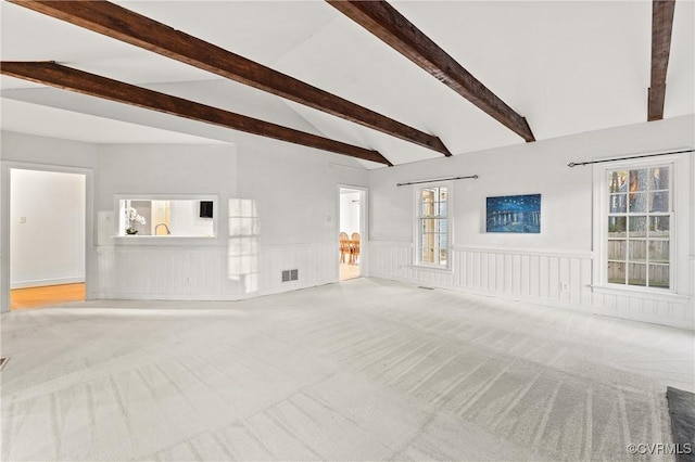 unfurnished living room featuring carpet flooring, lofted ceiling with beams, visible vents, and a wainscoted wall