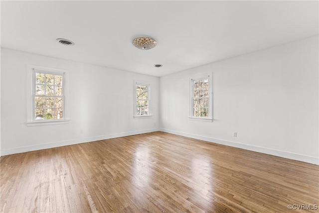 empty room with wood finished floors, visible vents, and baseboards