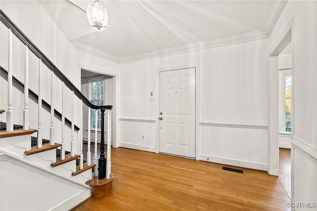 foyer entrance with plenty of natural light, visible vents, light wood finished floors, and ornamental molding