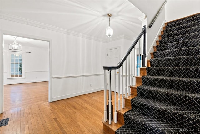 staircase with visible vents, baseboards, ornamental molding, an inviting chandelier, and hardwood / wood-style flooring