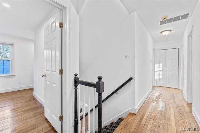 hallway featuring an upstairs landing, visible vents, light wood finished floors, and baseboards