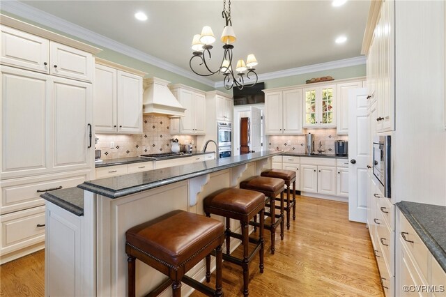 kitchen with light hardwood / wood-style floors, a breakfast bar, hanging light fixtures, a chandelier, and a kitchen island with sink