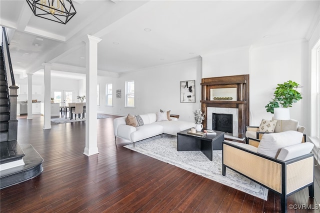 living room featuring hardwood / wood-style floors, ornate columns, ornamental molding, beam ceiling, and a chandelier