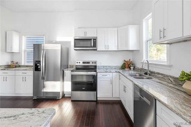 kitchen with sink, appliances with stainless steel finishes, dark hardwood / wood-style flooring, light stone counters, and white cabinetry