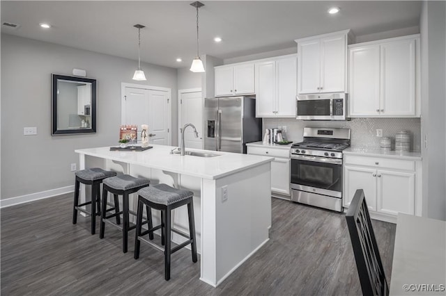 kitchen with white cabinets, stainless steel appliances, hanging light fixtures, and a center island with sink