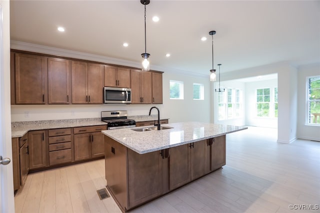 kitchen featuring stainless steel appliances, sink, light stone counters, decorative light fixtures, and an island with sink