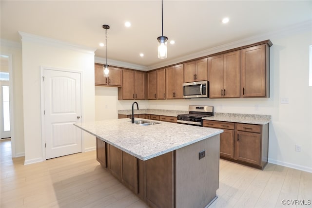 kitchen featuring sink, light stone counters, appliances with stainless steel finishes, decorative light fixtures, and a kitchen island with sink