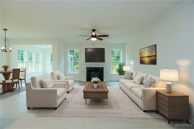 living room with a wealth of natural light, ceiling fan with notable chandelier, light hardwood / wood-style flooring, and crown molding