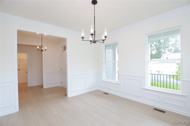 empty room featuring light hardwood / wood-style flooring, a chandelier, ornamental molding, and plenty of natural light