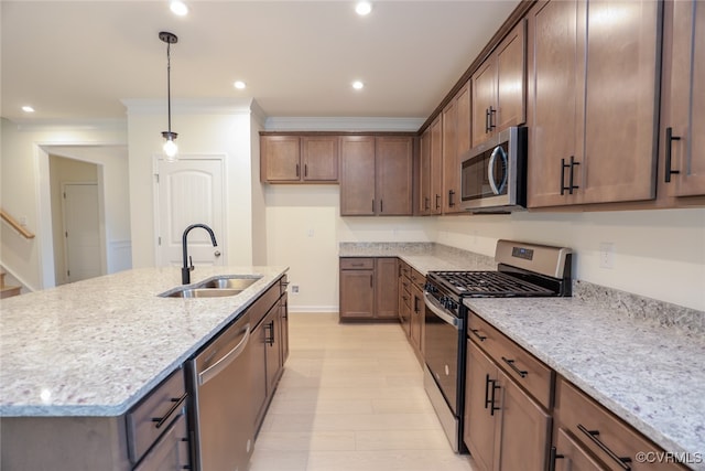 kitchen featuring light stone counters, a center island with sink, appliances with stainless steel finishes, hanging light fixtures, and sink