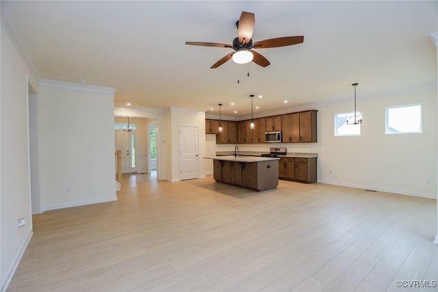 kitchen with sink, appliances with stainless steel finishes, an island with sink, hanging light fixtures, and light wood-type flooring