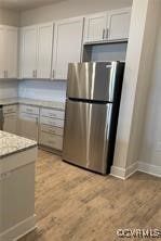 kitchen with white cabinets, light hardwood / wood-style floors, and stainless steel refrigerator