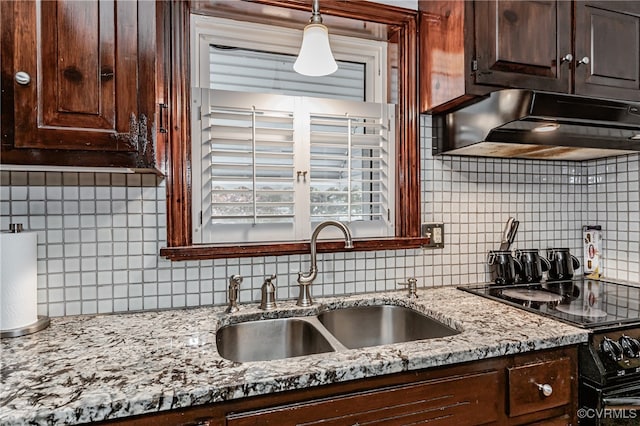 kitchen featuring sink, light stone counters, backsplash, hanging light fixtures, and black range