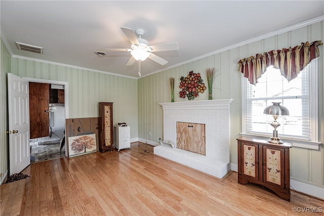 living room featuring ceiling fan, a brick fireplace, light hardwood / wood-style floors, and crown molding