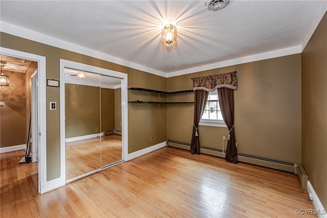 unfurnished bedroom with a textured ceiling, a baseboard heating unit, hardwood / wood-style flooring, and a closet