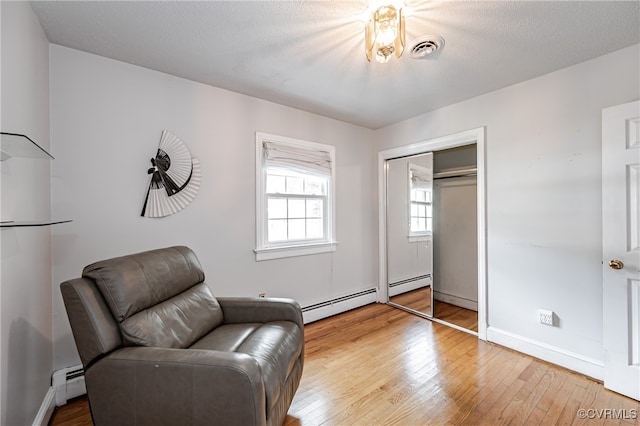 sitting room with wood-type flooring, a baseboard radiator, and a textured ceiling