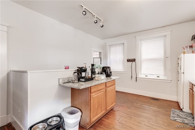 kitchen featuring light wood-type flooring, light stone counters, and white fridge