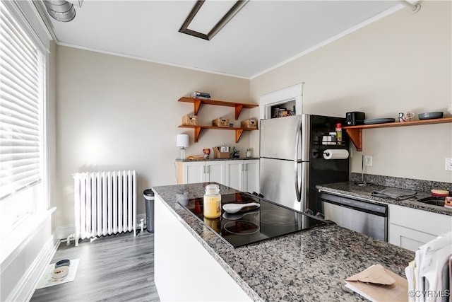 kitchen featuring dark hardwood / wood-style flooring, stainless steel appliances, radiator, white cabinets, and crown molding