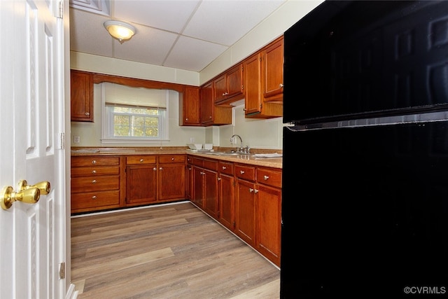 kitchen with light hardwood / wood-style floors, black refrigerator, sink, and a drop ceiling