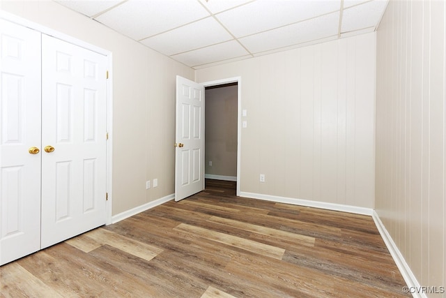 unfurnished bedroom featuring a closet, a drop ceiling, and wood-type flooring