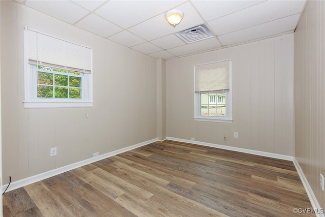 unfurnished room featuring a wealth of natural light, a paneled ceiling, hardwood / wood-style flooring, and wooden walls